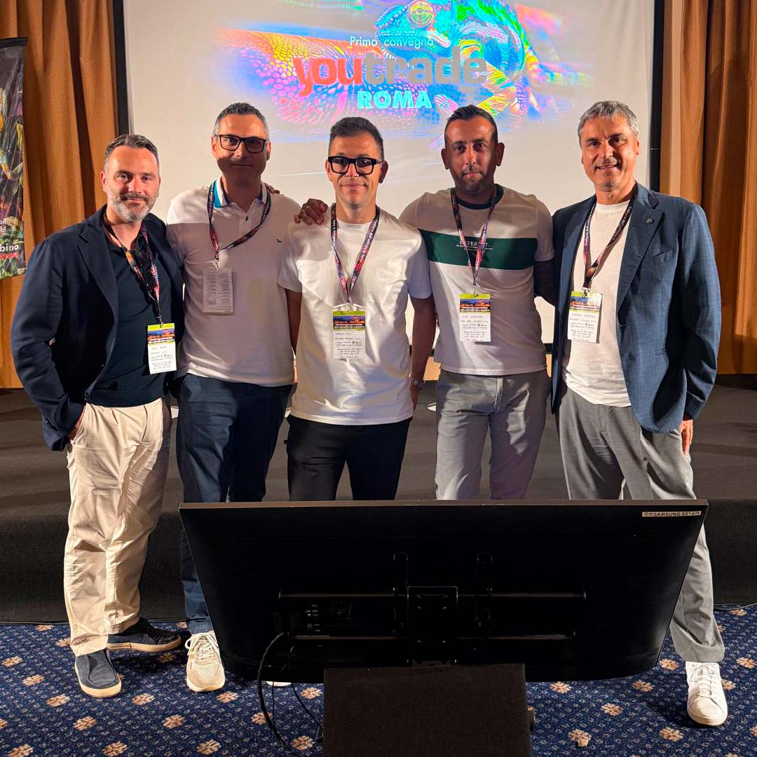 Five men with conference badges pose together on a stage in front of a colorful screen showing 'youtrade ROMA'.