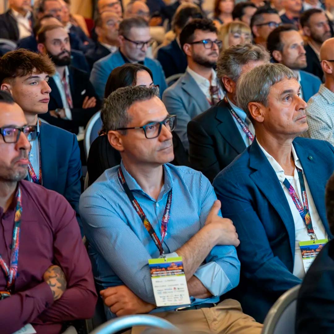 Group of professionals seated in a conference auditorium, attentively watching a presentation.
